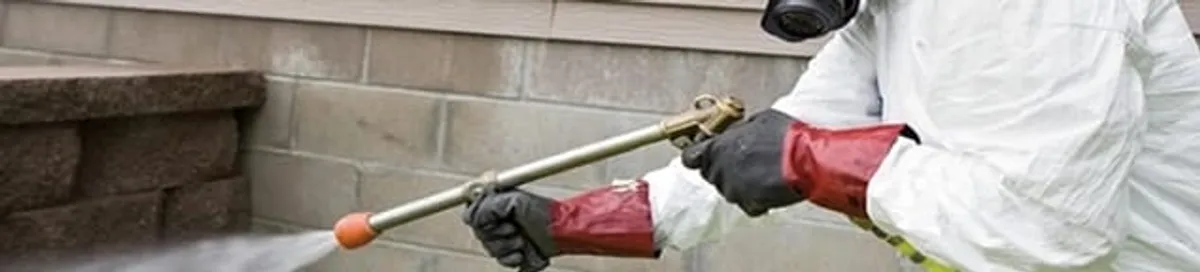 Pest control technician applying exterior insect treatment along a home foundation in Seattle, WA