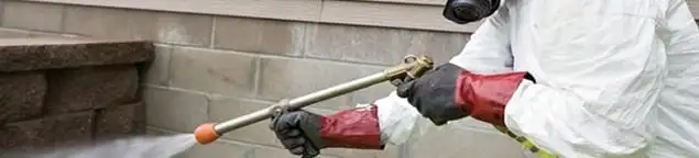 Pest control technician applying exterior insect treatment along a home foundation in Seattle, WA