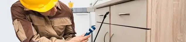 Roach exterminator applying treatment under kitchen cabinets in Seattle, WA