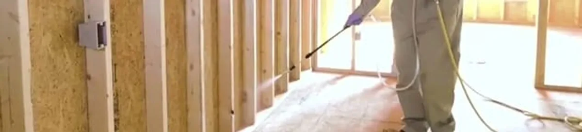 Termite treatment technician applying spray along framing and unfinished walls in Seattle, WA